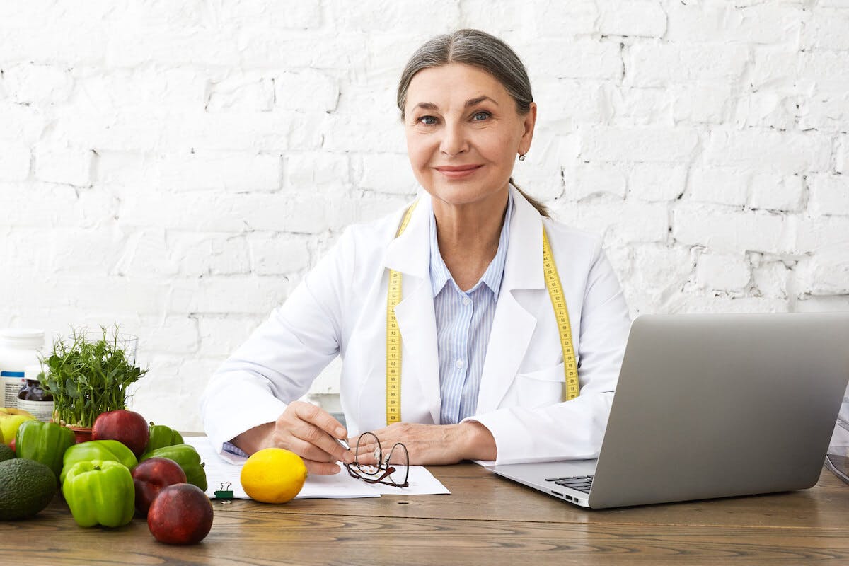 Online nutrition coach with a tape measure on her shoulders smiling to the camera